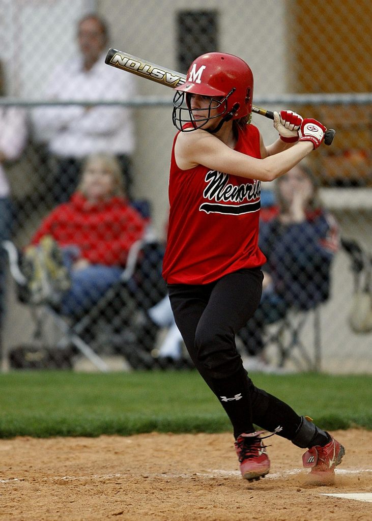 Young female softball player in red uniform swinging a bat during a game outdoors.